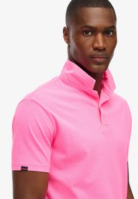 Polo à manches courtes de couleur rose vif, doté d'un col à boutons, d'un tissu doux et d'un petit logo sur la manche gauche.