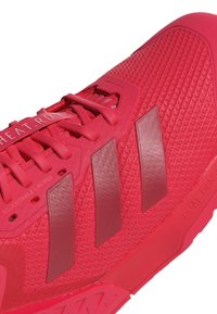 Scarpa da sport rossa con parte superiore in mesh testurizzato, tre strisce opache, lacci regolabili e suola in gomma solida con un motivo di battistrada unico.