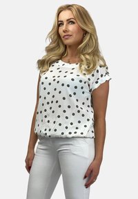 Biała krótka bluzka z zielonymi kropkami, luźny krój, okrągły dekolt i elastyczny dół. W zestawie z białymi spodniami.