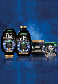 Prodotti per la cura dei capelli Garnier Ultra Dolce in bottiglie nere e un barattolo, con disegni floreali blu e dettagli dorati. Include shampoo e balsamo.