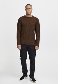 Pulover tricotat maro cu un model texturat, gât rotund, mâneci lungi, asortat cu pantaloni negri și sneakers negri cu dungi albe.