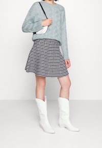 Ljust blå stickad tröja, svart och vit rutig utsvängd kjol, vita knähöga cowboystövlar och en liten vit axelväska.