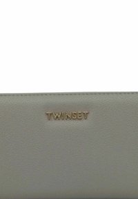 Portafoglio in pelle grigia con superficie testurizzata e logo "TWINESET" in rilievo dorato. Forma rettangolare con design slim e dettagli minimi.