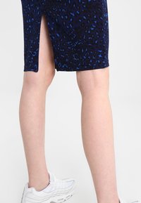 Marinblå kjol med ett leopardsmönster, med en sidofrans. Bärs med vita träningsskor. Slät textur och figurvänlig design.