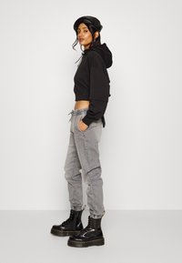 Svart avkortet hettegenser med snor, kombinert med grå tapered joggebukser. Modellen har på seg skinnende svarte snøreboots med kraftige såler.