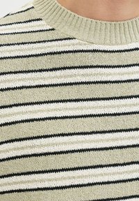 Gros plan d'un pull en maille beige avec des rayures horizontales noires et blanches, un col côtelé et une texture de tissu visible sur la partie supérieure de la poitrine d'une personne.