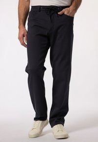 Czerwone spodnie w ciemnogranatowym kolorze o luźnym kroju, z elastycznym paskiem ze sznurkiem i bocznymi kieszeniami, w połączeniu z białymi trampkami. Gładka tekstura materiału.