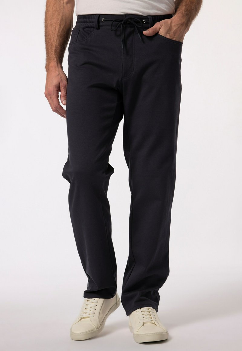 Czerwone spodnie w ciemnogranatowym kolorze o luźnym kroju, z elastycznym paskiem ze sznurkiem i bocznymi kieszeniami, w połączeniu z białymi trampkami. Gładka tekstura materiału.