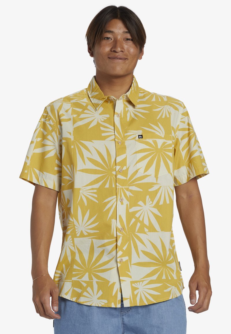Camicia a maniche corte di colore giallo con motivo a foglia di palma bianca, realizzata in tessuto leggero. Design con bottoni e una piccola etichetta con logo.