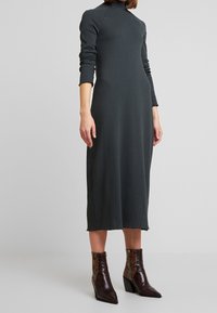 Robe midi côtelée de couleur gris foncé avec des manches longues et un col haut. Présente un ourlet effiloché discret et est associée à des bottes à bout pointu en imprimé serpent.