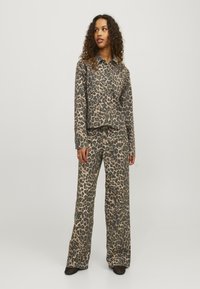 Leopard print shirt and pants set in beige and dark brown, featuring a boxy design and loose fit, made from soft fabric with minimal hardware.