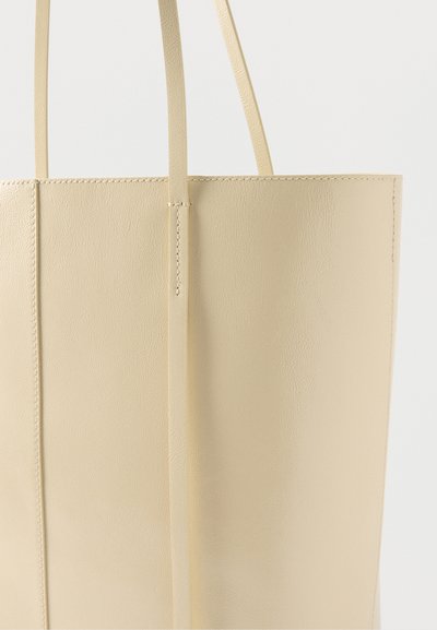 Μπεζ δερμάτινη τσάντα tote με λεπτούς ιμάντες ώμου και εμφανείς ραφές, σε απλό ανοιχτό φόντο.