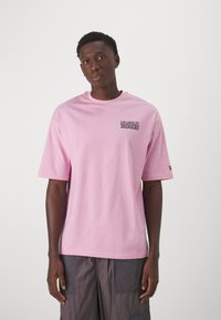 Camiseta de algodón rosa con el logotipo de "Los Angeles Dodgers" en negro en el pecho, cuello redondo y mangas cortas rectas.