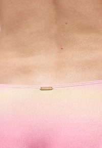 Κοντινή λήψη της κάτω μέσης και της ζώνης παντελονιού από ύφασμα ροζ διαβάθμισης με μικρή χρυσή ετικέτα με την επιγραφή «Hollister».