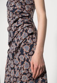 Robe bleu marine avec motif cachemire en tons bleus et rouille, texture froncée sur le côté et silhouette ajustée.