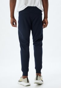 Marineblauwe joggers met een elastische tailleband, taps toelopende benen en een gestructureerde stof, gecombineerd met lichte sneakers met zwarte accenten.