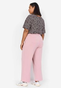 Lös sittande blommig blus i svart och rosa, kombinerad med högmidjade rosa vida byxor. Outfiten inkluderar vita atletiska skor.