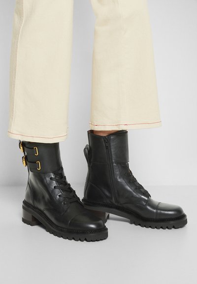 Black leather ankle boots with a matte finish, featuring laces, side zipper, and gold buckles. Thick, textured rubber sole with a block heel.