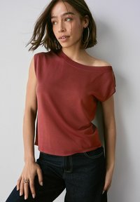 Top rojo acanalado, off-the-shoulder, con mangas cortas y un ajuste relajado. Combinado con pantalones vaqueros oscuros de tiro alto.