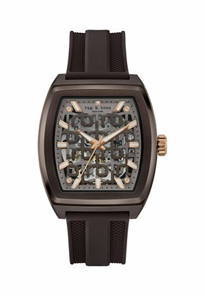 Reloj esqueleto Rag & Bone de color marrón oscuro, con corona, agujas e índices horarios en oro rosa y una correa de caucho texturizada.