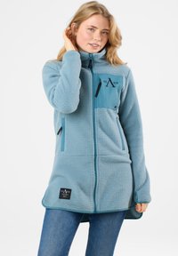 Giacca in fleece blu chiaro con zip intera, colletto alto e tasca frontale. Presenta dettagli neri e una toppa con logo sull'orlo. Tessuto morbido.