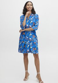 Rochie florală albastră cu un design cu nasturi în față, mâneci trei sferturi și talie legată. Prezintă flori multicolore pe un fundal vibrant.