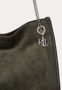 Žalia zomšinė rankinė su tekstūruotu paviršiumi, turinti sidabrines grandines ir metalinį logotipo akcentą. Stilingas dizainas, erdvus vidus.