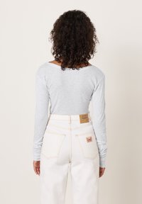 Svijetlosivi top s dugim rukavima i izrezom u obliku čamca, uparena s bijelim trapericama visokog struka, ukrašenim smeđom oznakom i crvenim detaljima šavova.