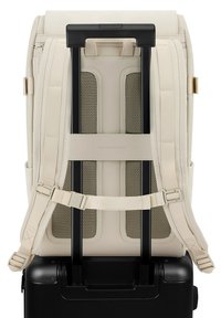 Beige ryggsäck fäst vid en svart väskvagn, med vadderade remmar, meshventilation och justerbara spännen för komfort och stöd.