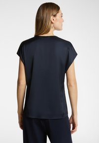 Blusa blu navy con maniche corte, tessuto leggero e liscio, colletto arrotondato e vestibilità morbida, vista da dietro.