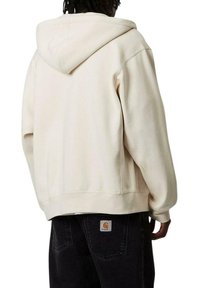 Sudadera color crema con capucha ajustable, que presenta un corte holgado y una textura suave. La vista trasera muestra un diseño limpio y sin adornos.