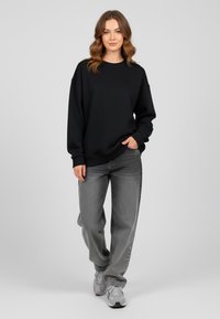 Felpa nera con colletto rotondo e spalle scese, abbinata a jeans grigi dalla vestibilità ampia e sneakers grigie. Design semplice e informale.