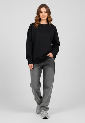 Sweat-shirt noir à col rond et épaules tombantes, associé à un jean gris ample et des baskets grises. Design simple et décontracté.