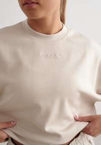 Sweatshirt beige chiaro con collo a giro, caratterizzato da un logo ricamato. Tessuto morbido, vestibilità comoda e design leggermente oversize.
