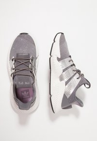 Grå sportskor med en texturerad tygöverdel, silverdetaljer och en mönstrad vit sula. Har snören och en vadderad krage.