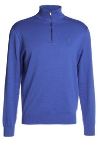 Pull en tricot bleu avec un col zippé à mi-hauteur, des poignets et un ourlet côtelés, et un petit logo vert sur la poitrine gauche. Texture douce.