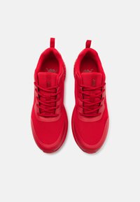Red athletic shoes with a mesh upper and rubber sole. Features include round laces and fabric loops at the heel for easy wear.