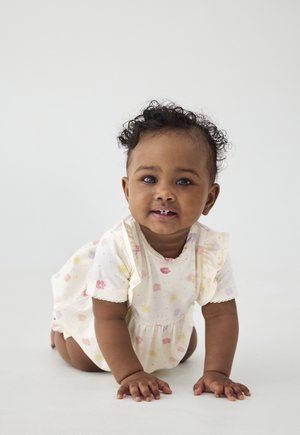 Lichtcrème romper met bloemmotieven in pasteltinten. Ruches aan de mouwen en gegolfde randen. Kind kruipt op een effen achtergrond.