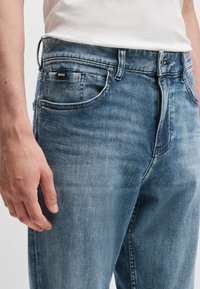 Lichtblauwe denim jeans met een vervaagde afwerking. Kenmerken zijn onder andere vijf zakken, een ritsopening en een zwart "BOSS" label op de tailleband.