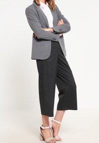 Šedý blazer přes růžovou košili, doplněný tmavými kulotami a béžovými sandály na podpatku. Hladká tkanina, střih na míru a minimalistický design.