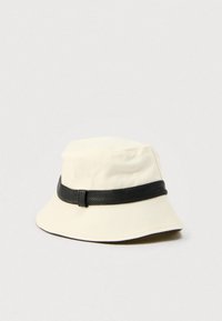 Καπέλο τύπου bucket σε εκρού χρώμα με μαύρη ταινία από ψεύτικο δέρμα. Διαθέτει απαλή υφή υφάσματος και φαρδύ γείσο. Το πάνω μέρος έχει στρογγυλεμένο σχέδιο κορυφής.