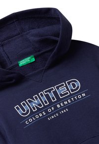 Tmavě modrá mikina s klokaní kapsou, s bílým a modrým textem "UNITED COLORS OF BENETTON" a zelenou cedulkou uvnitř límce.