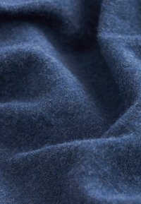 Tessuto di lana blu scuro con una superficie morbida e testurizzata e sottili fibre visibili, disposte in pieghe e creste morbide.