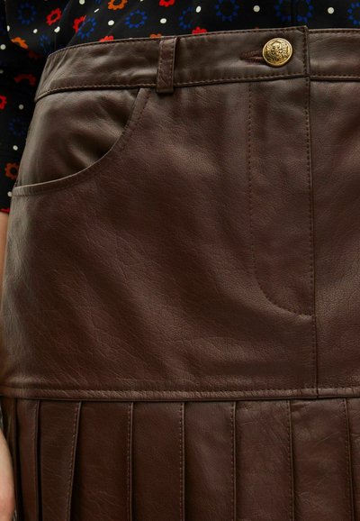 Bruine leren rok met knoopsluiting, voorkantzak en geplooid ontwerp aan de onderkant, met een gestructureerde afwerking.
