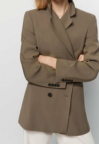 Blazer marrone su misura con design doppiopetto, rever a punta e sei bottoni neri. Il tessuto è liscio con una vestibilità strutturata.