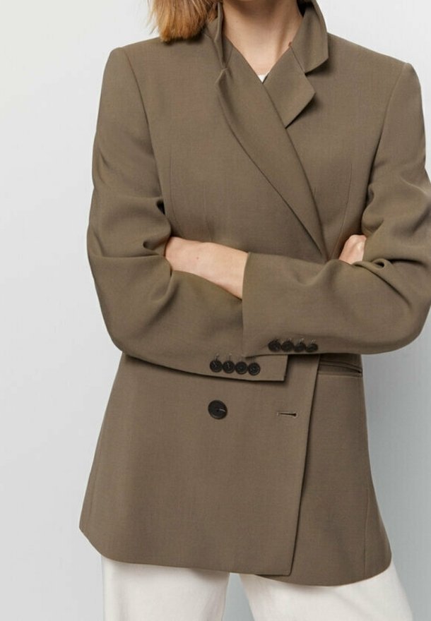 Blazer marrone su misura con design doppiopetto, rever a punta e sei bottoni neri. Il tessuto è liscio con una vestibilità strutturata.