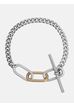 Bracelet chaîne en argent avec un maillon ovale en or et un fermoir à bascule en argent sur un fond uni.