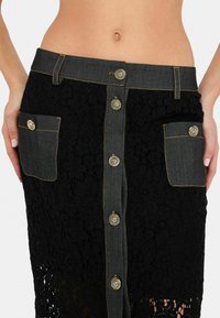 Jupe en dentelle noire avec des accents en denim, dotée de boutons dorés, de motifs floraux et de poches avant. Design mi-long avec une finition texturée.