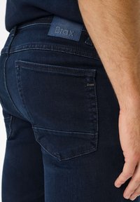Jeans in denim blu scuro con una trama liscia. Caratterizzati da una tasca posteriore cucita, un'etichetta in pelle marchiata e un design aderente.