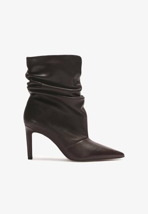 Tamno smeđi kožni školski čizme s uskim vrhom i tankim visokim potpeticama na bijeloj pozadini.